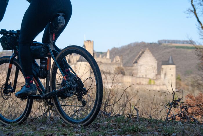 A mountain bike rides past, with Vianden Castle visible in the background.